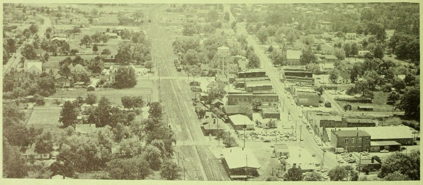 Black-and-white aerial photo of downtown Apex in the early 1960s: the railroad tracks, Salem Street business blocks, the water tower and tree-covered neighborhoods